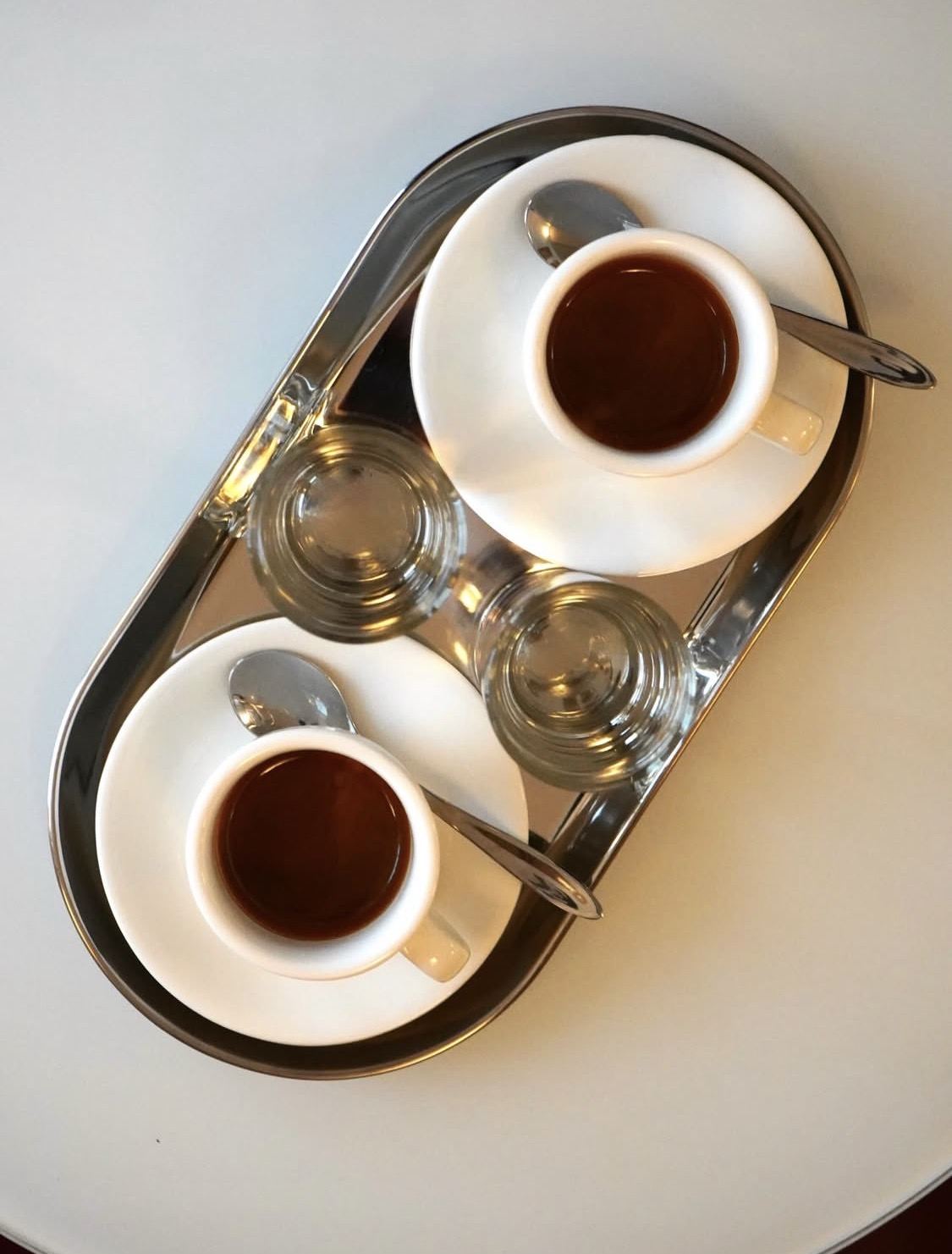 Two espresso cups and glassware on a polished steel tray at Bar Tatti, an intimate Italian caf&eacute; bar in central Copenhagen.